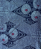 8114: Center closeup. 1970s Ohshima Tsumugi silk, geometric patterned textile featuring navy blue and light blue geometric diamond motifs with stylized floral or medallion shapes in pale blue and small red centers.