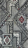 A close-up of a patterned textile featuring geometric shapes and ornate borders in black, gray, white, and muted red accents.