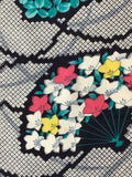 81062 meisen silk 1930s A close-up of a patterned textile featuring white, pink, and yellow flowers with teal leaves on a black background, layered over a gray and white geometric lattice pattern.