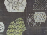 81202 Doro Ohshima Tsumugi Silk Close-up of a woven textile pattern with abstract floral and geometric motifs in off-white and pale yellow-green on a dark charcoal background.