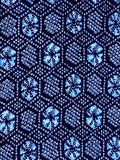 81332: A close-up of a batik type  fabric pattern featuring light blue and white geometric hexagonal motifs ligher blue alternating concentrics on a dark navy blue background.
